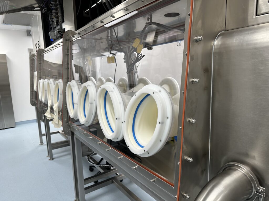 A stainless steel glovebox isolator line with glove ports, in a cleanroom